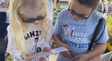 Two young blind girls look at a Braille card together.